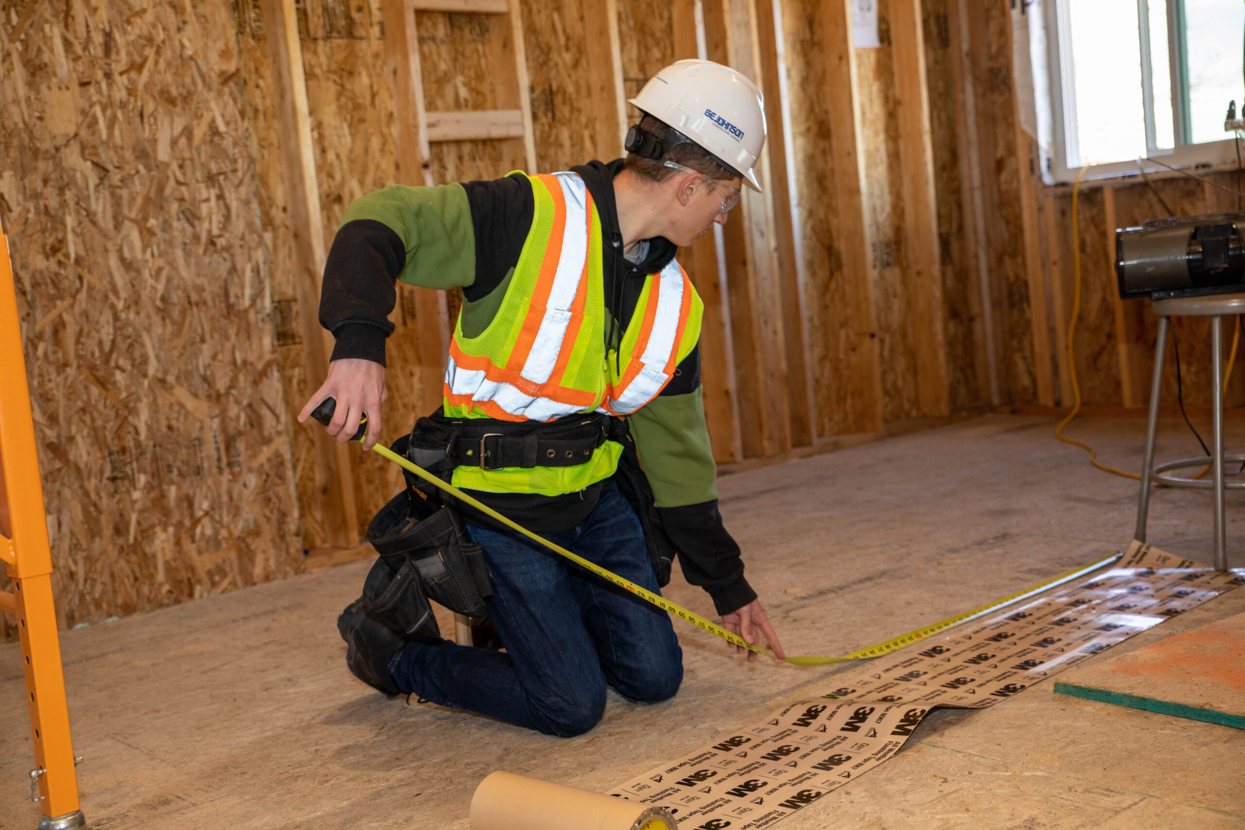 Student in construction gear using a tape measure