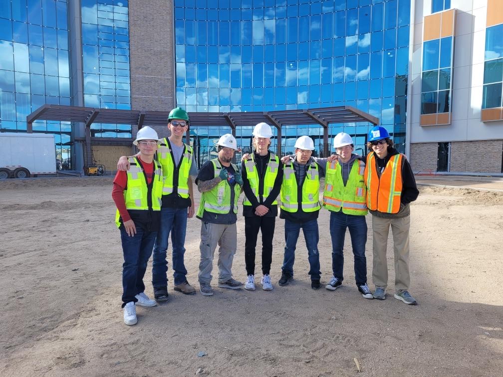 Students in vests and hardhats standing in front of a tall building